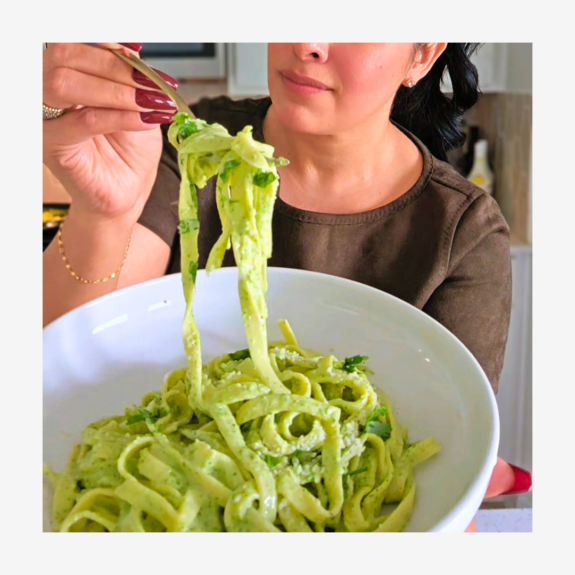 Woman holding a ceramic plate filled with creamy poblano tagliatelle. She is holding up the fork with pasta