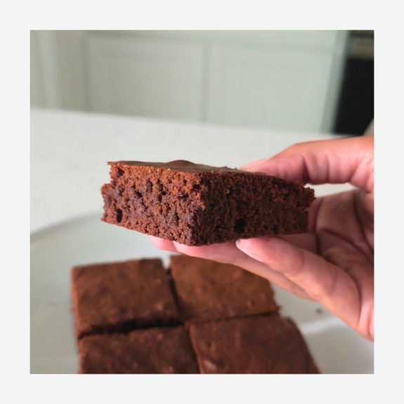 White plate in the background with four brownies. Closeup of hand holding a brownie